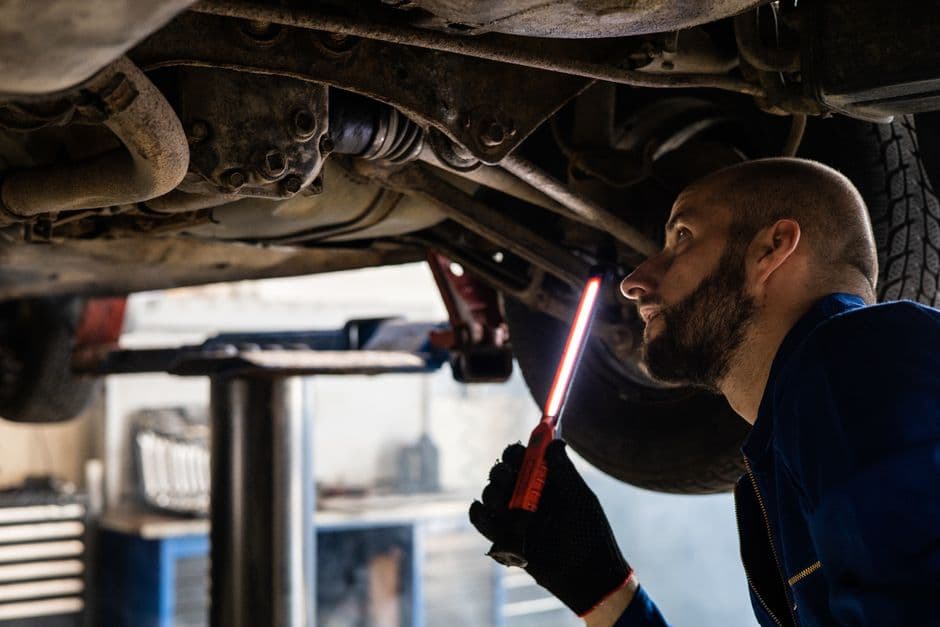Mechanic using a light to inspect a vehicle's undercarriage