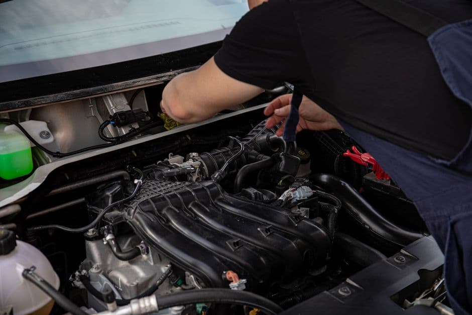 Mechanic inspecting a car engine's serpentine belt during a maintenance check