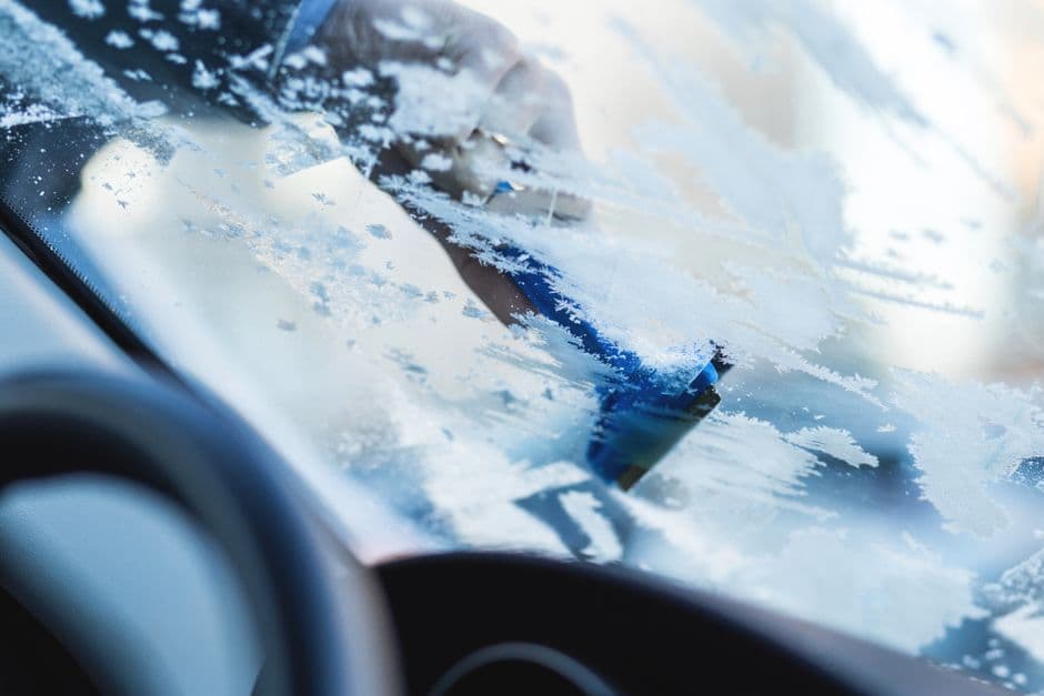 Driver scraping ice off a car windshield during winter car maintenance