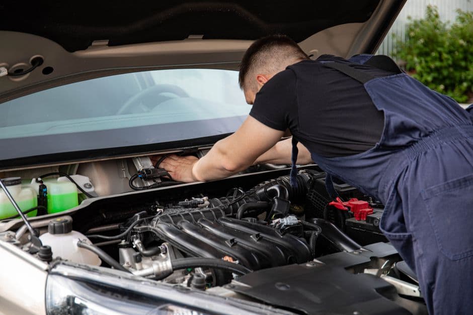 Mechanic performing car engine maintenance under the hood of a vehicle