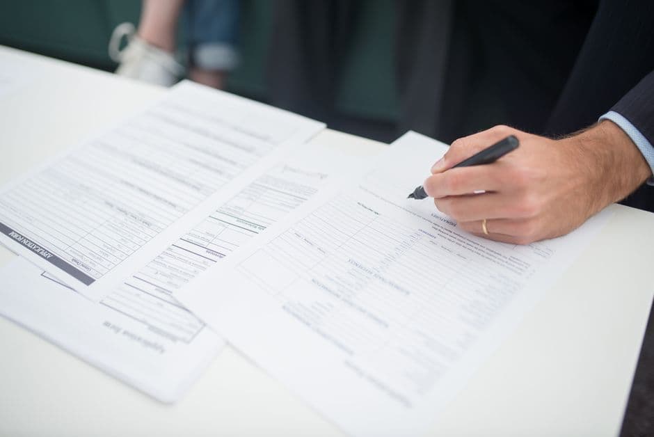 Hand signing a car insurance policy document at a desk