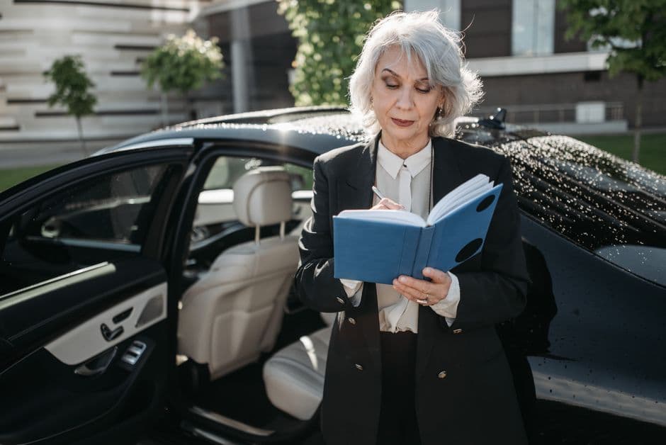 Owner filling in a printable car maintenance log in a notebook beside a car