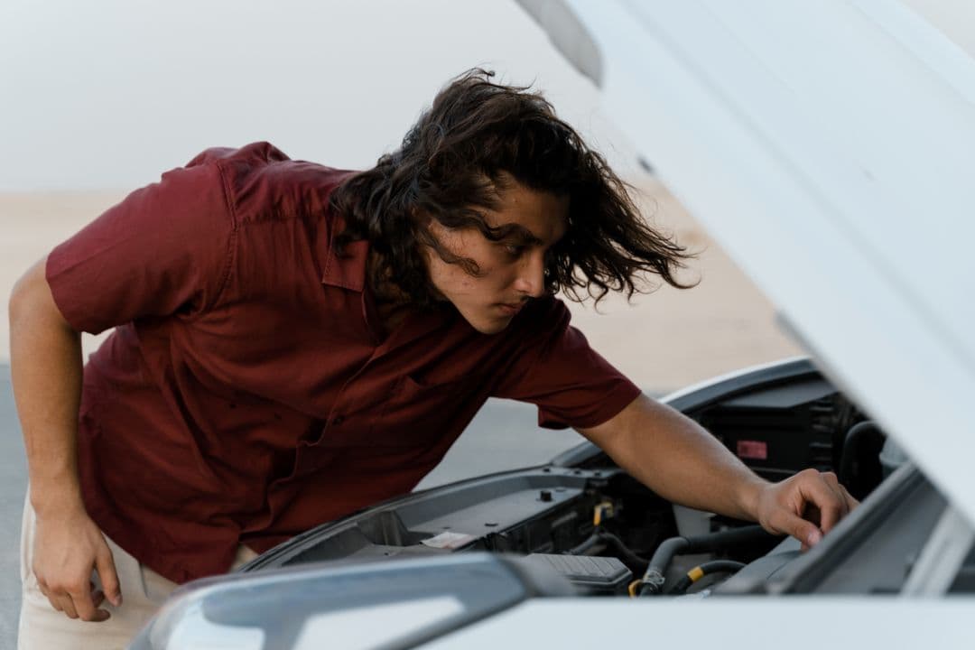 A beginner checking under a car hood, the starting point for basic car maintenance