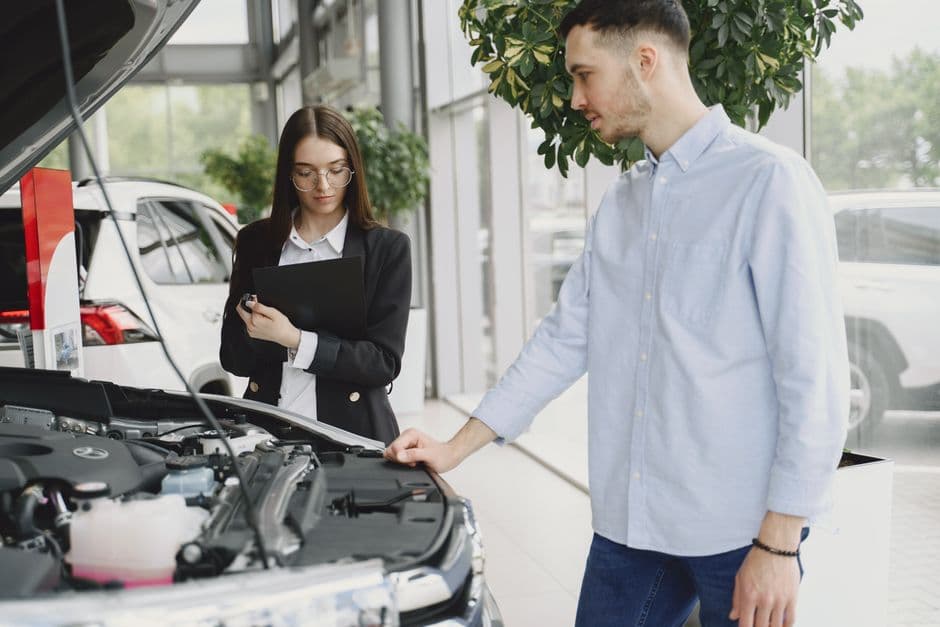 Mechanic and customer examining a car in a dealership service bay, discussing a recall repair
