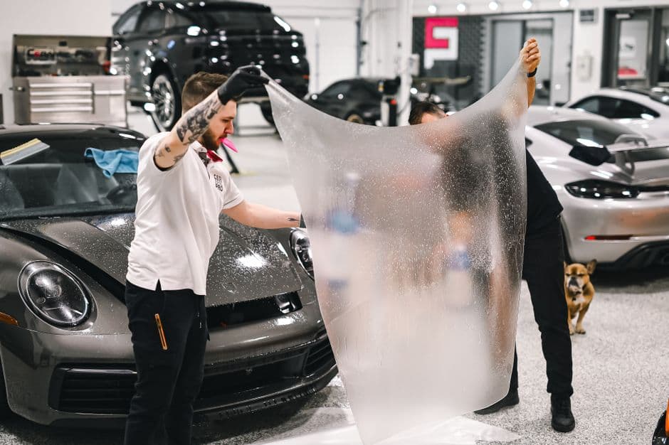 Two technicians applying paint protection film to a car in a detail shop