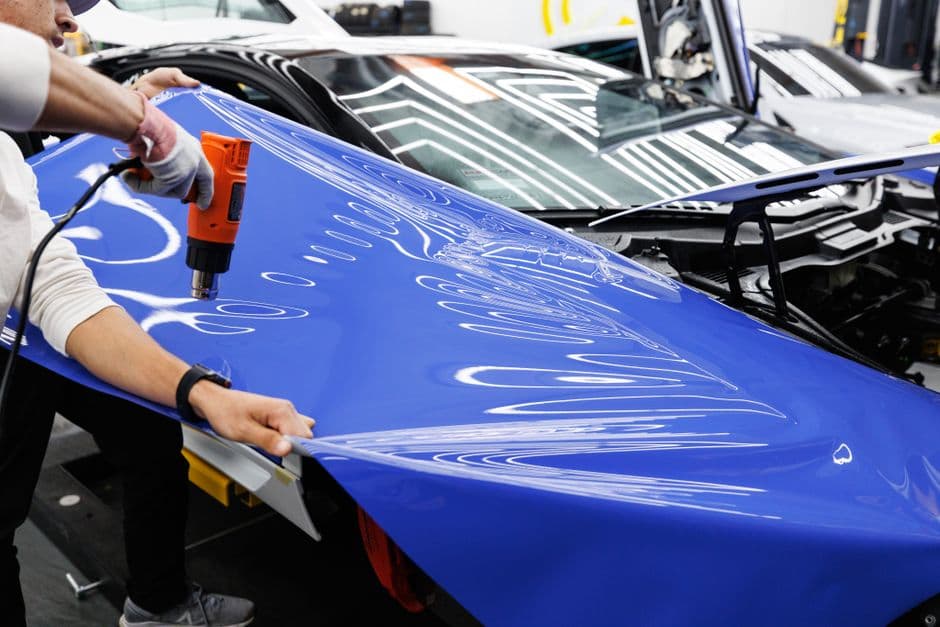 Technician using a heat gun to install vinyl wrap on a car body panel