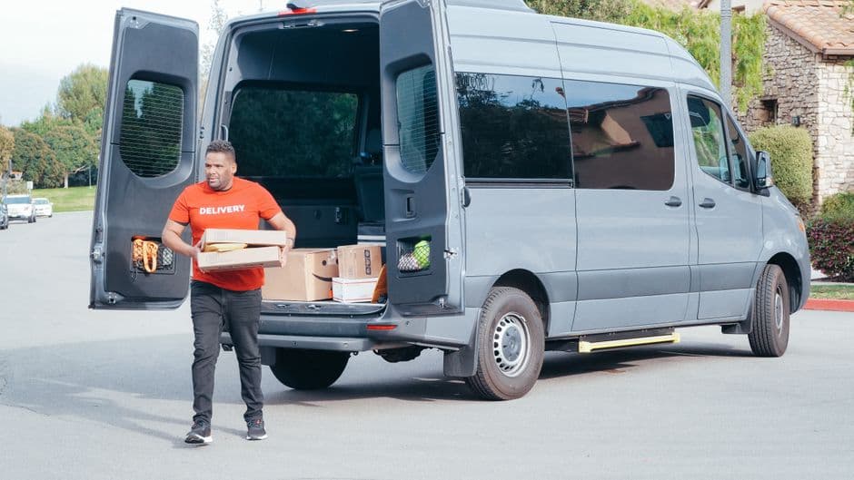 Courier delivering packages from a cargo van on a daily route, the kind of duty cycle cargo van maintenance has to account for