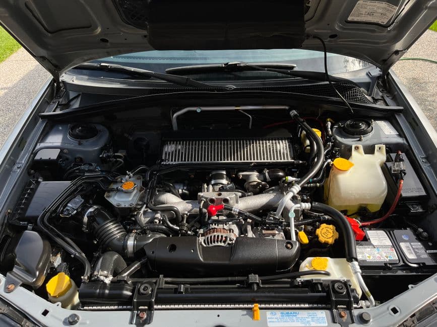 Close-up view of car engine components under the hood, including the alternator and drive belt