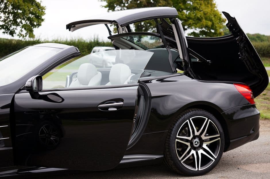 Side view of a convertible car with its soft top folded down, showing the top's stack and mechanism