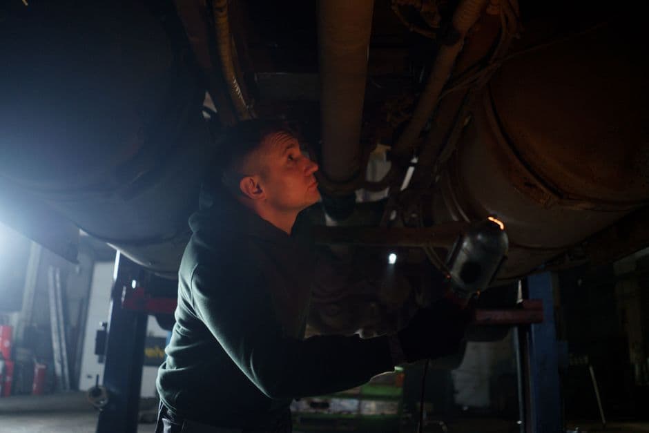 Mechanic inspecting a vehicle's underbody for CV axle and driveshaft wear in a garage