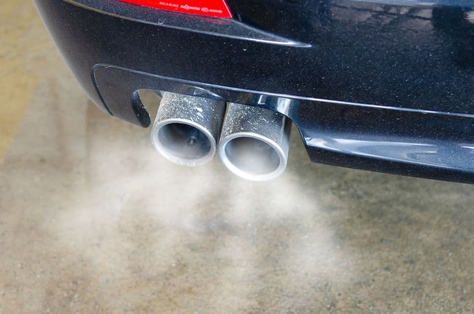 Close-up of a vehicle exhaust pipe with visible exhaust smoke, related to diesel particulate filter and EGR maintenance