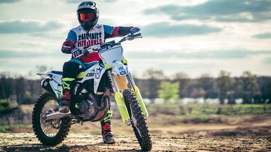 Dirt bike rider in full protective gear riding on a dusty off-road trail