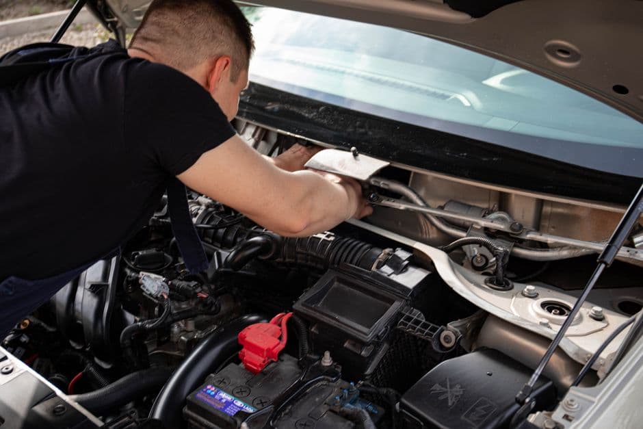 Person doing DIY car maintenance work under the hood to save on shop labor cost