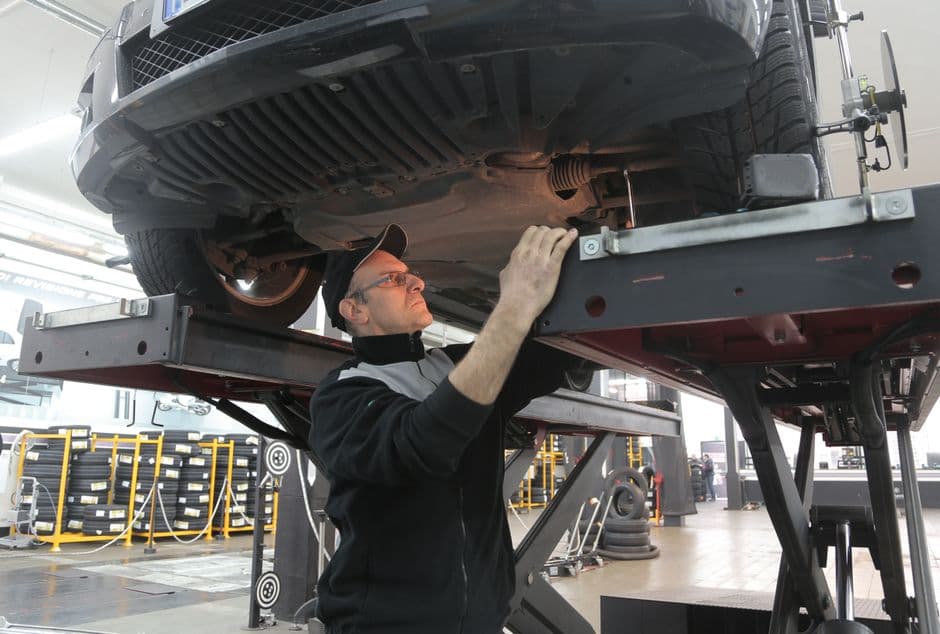 Mechanic inspecting the underside of a car on a lift, including the exhaust system