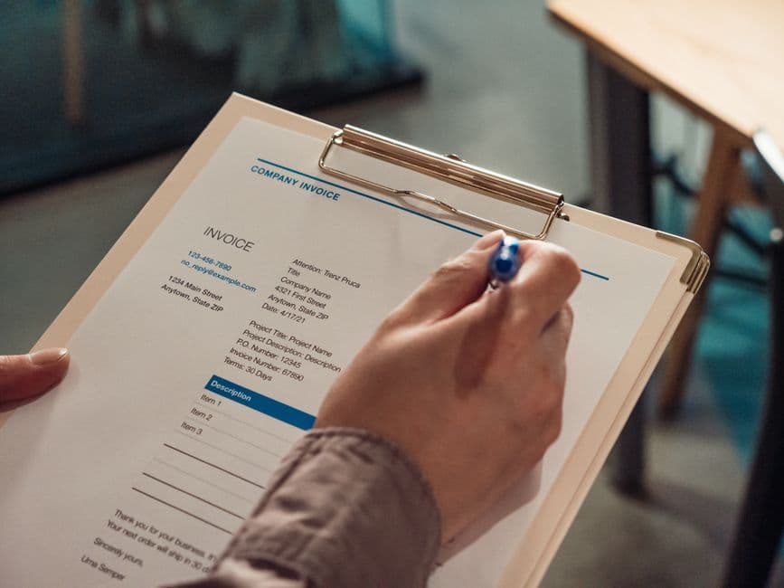 Hand holding a vehicle service invoice on a clipboard, the paperwork behind fleet maintenance records