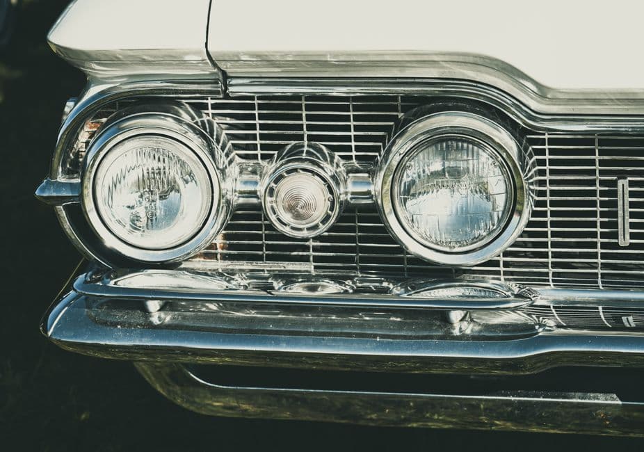 Detailed view of an older car's headlight and grille showing lens condition