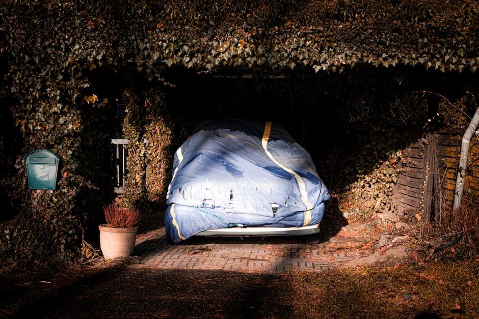 Car covered with a protective tarp in a driveway for long term storage