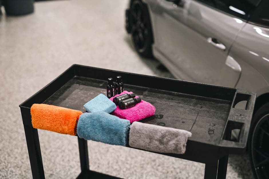 Microfiber drying towels and car detailing supplies laid out beside a car