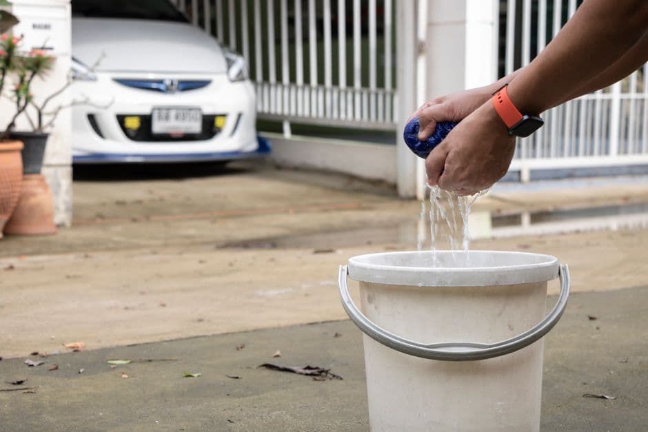 Washing a car by hand with a soapy mitt and bucket in a driveway