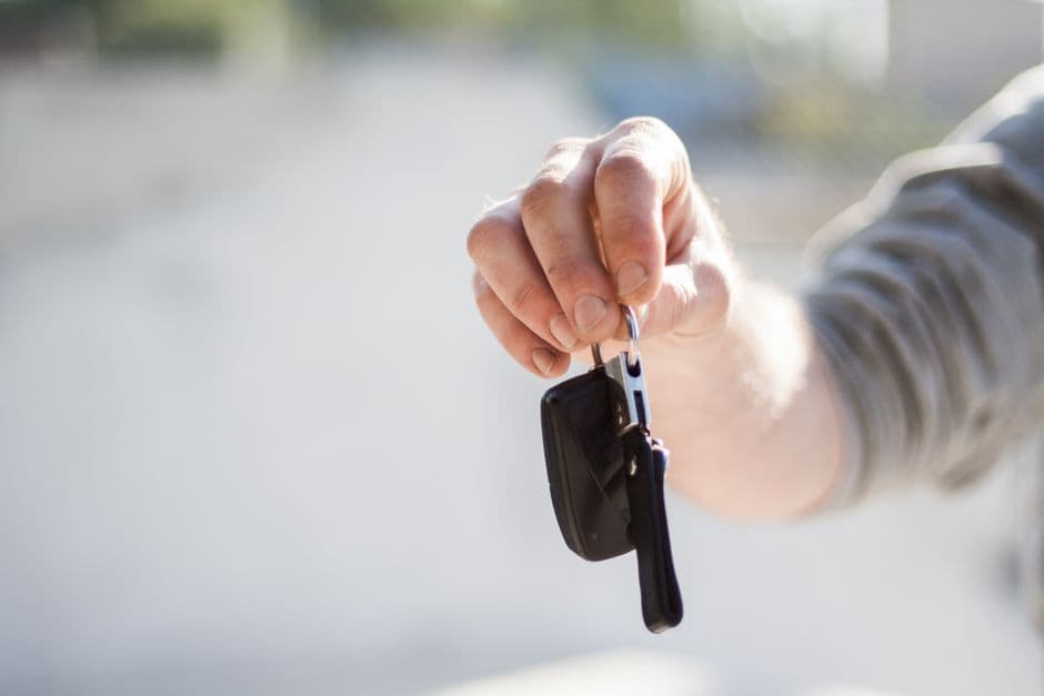 Hand holding a car key fob near a vehicle door handle