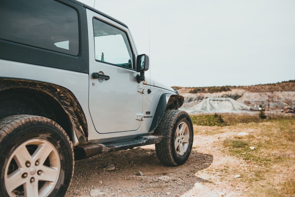 Jeep with lifted off-road suspension driving on a trail, showing the increased wheel travel a suspension lift provides