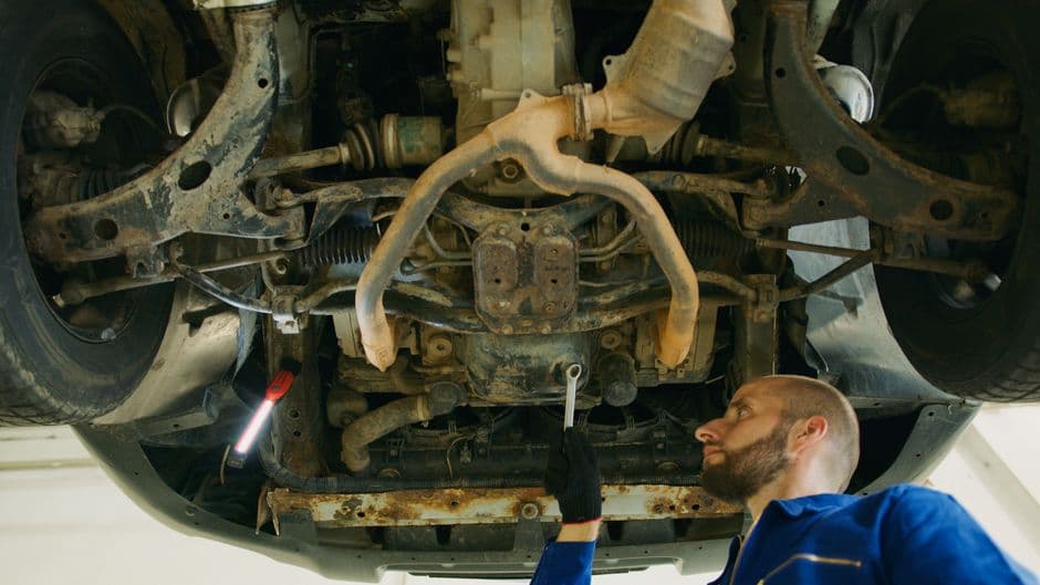 Mechanic inspecting a vehicle's undercarriage for rust and corrosion damage