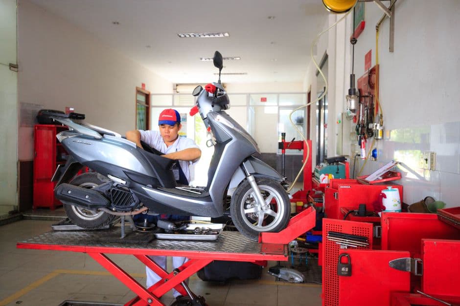 Mechanic performing routine scooter maintenance on a lift in an indoor repair shop