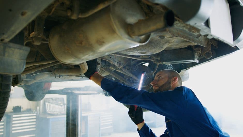 Mechanic inspecting the underside of a vehicle near the transmission during service