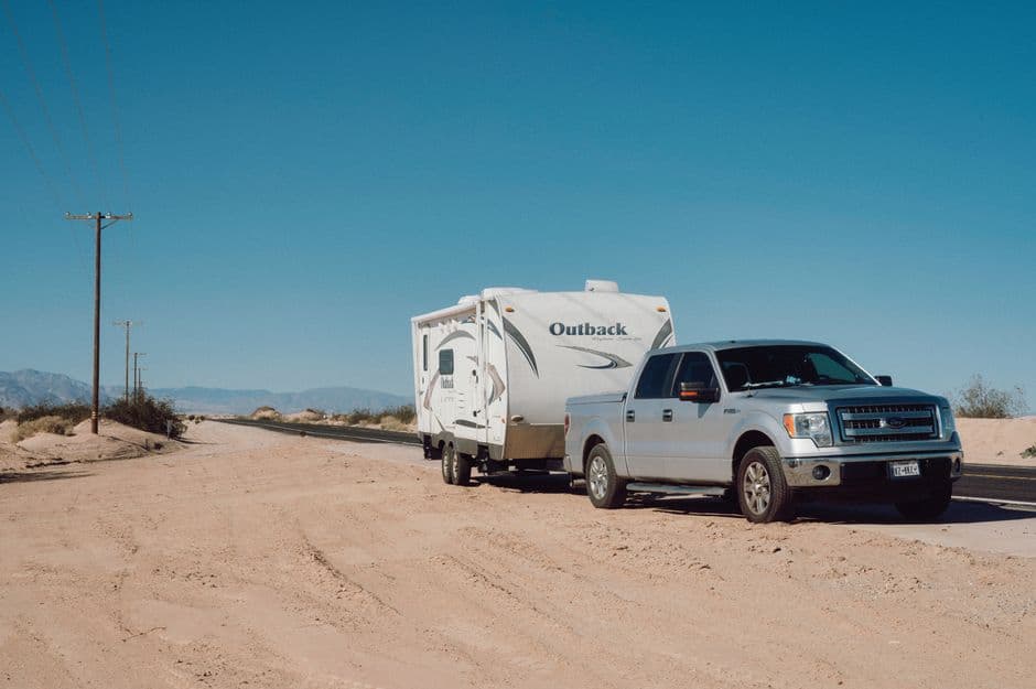 Truck towing a utility trailer on a desert road, illustrating trailer maintenance for towing