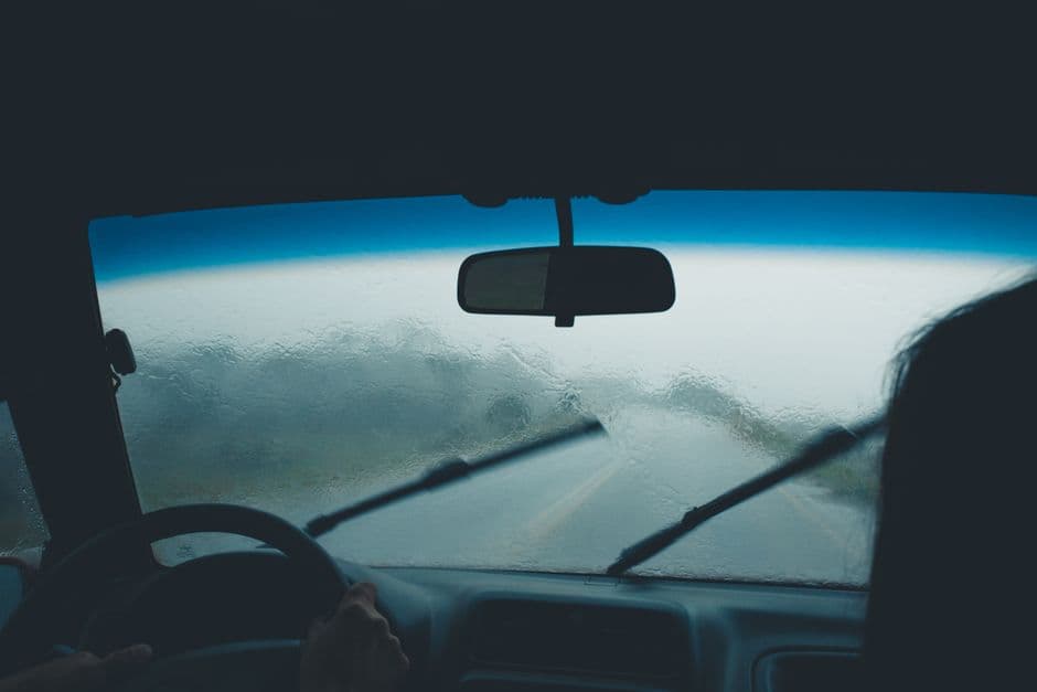 Rain covering a car windshield with the wipers running, showing the washer system at work in wet weather